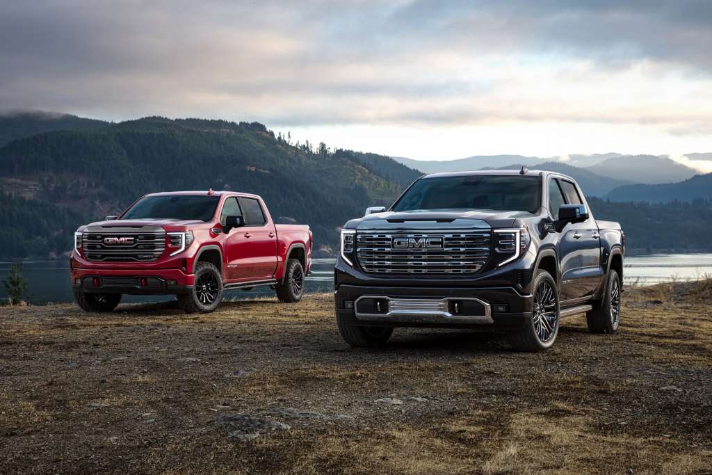 A black and a red 2024 GMC Sierras sitting in a field